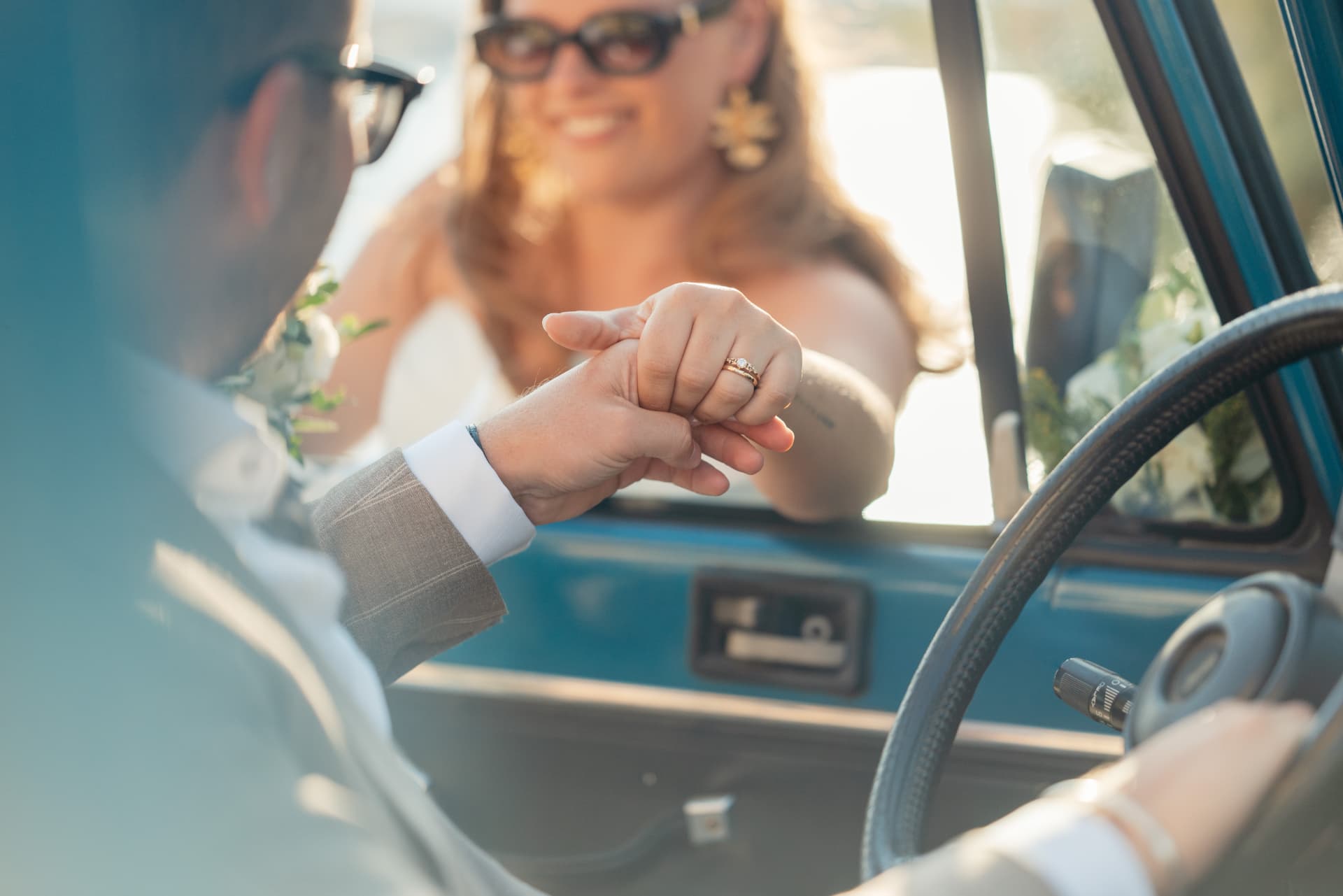 A groom kissing the bride's hand through the window of a vintage car