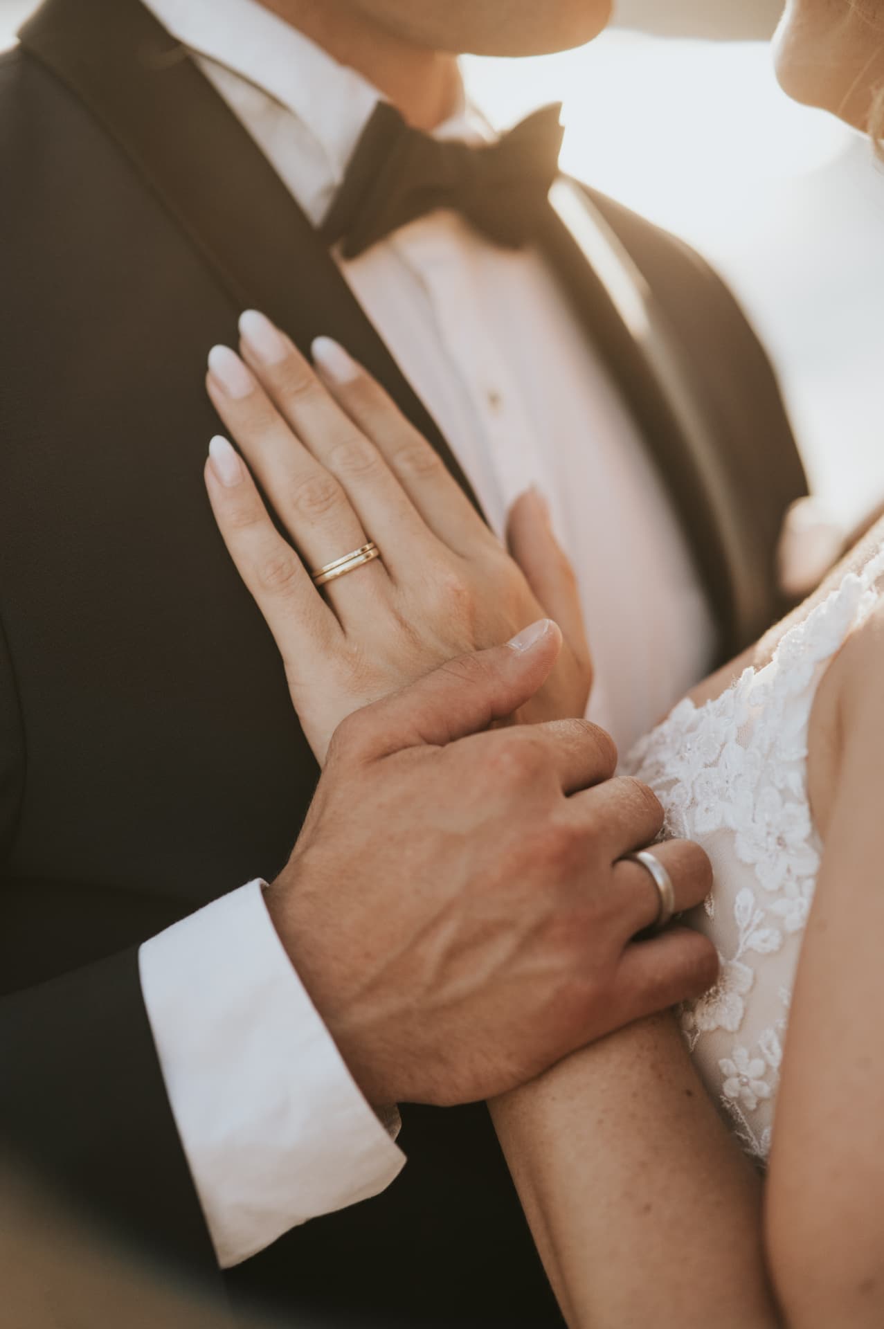 A groom's hand resting on the bride's, their rings catching the light