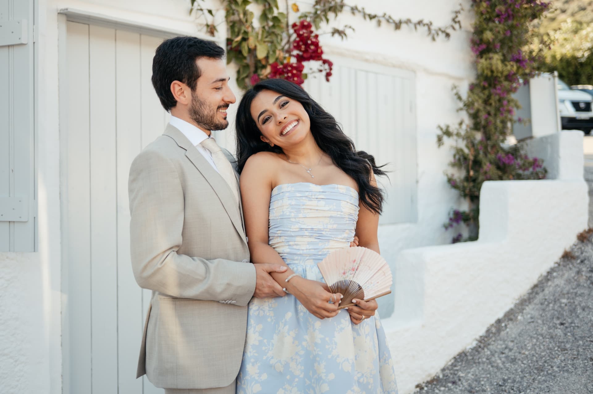 A couple laughing in front of a whitewashed Greek house