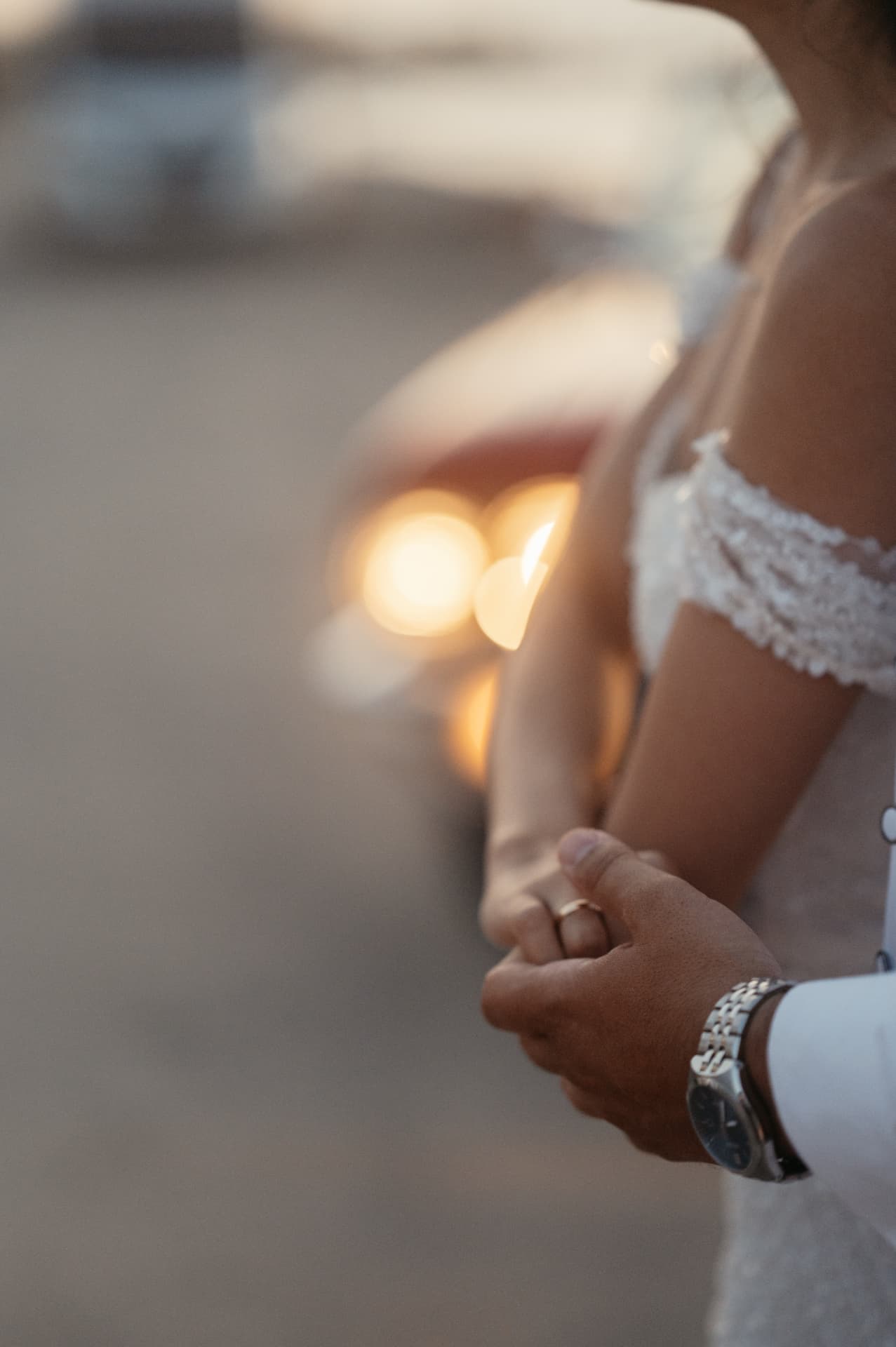 A couple holding hands in front of warm headlights at dusk
